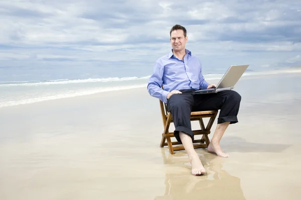 Επιχειρησιακό άτομο που κάθεται σε μια καρέκλα στην παραλία με laptop — Φωτογραφία Αρχείου