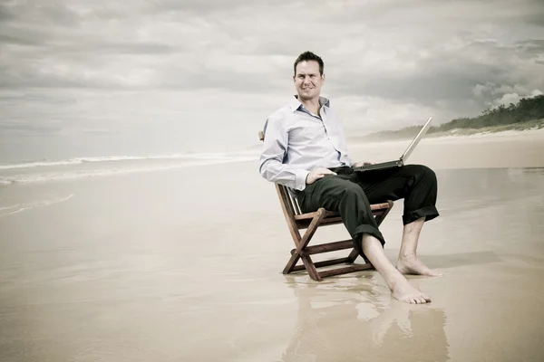 stock image Business man sitting on a chair on the beach with laptop