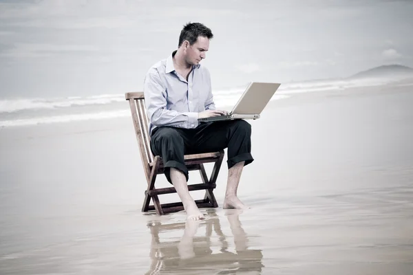 Ділова людина сидить на стільці на пляжі з ноутбуком — стокове фото