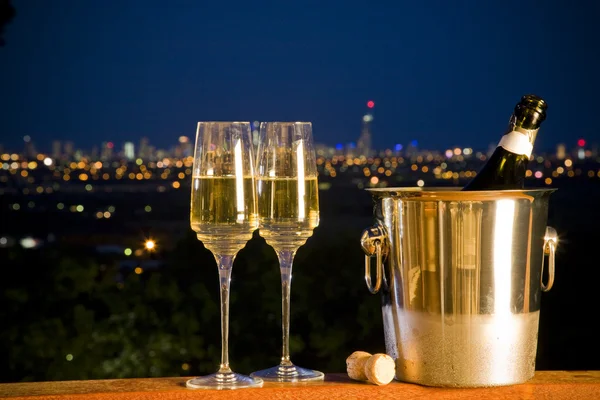 Champagne bottle and two glasses with night skyline in backgroun — Stock Photo, Image