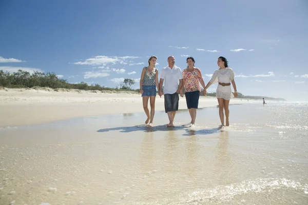 Семья ходит по пляжу держа руки — стоковое фото