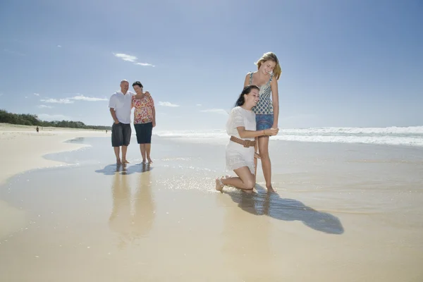 Schwestern betrachten Muschel am Strand mit Eltern im Hintergrund — Stockfoto