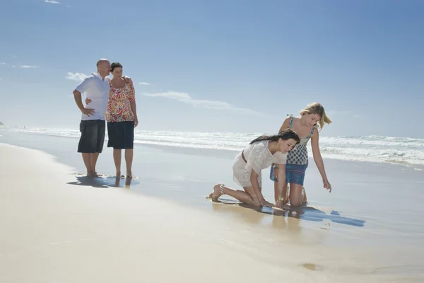 Sestry s rodiči v pozadí při pohledu na shell na pláži — Stock fotografie