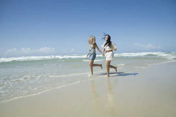 Zwei Schwestern laufen am Strand Händchen haltend — Stockfoto