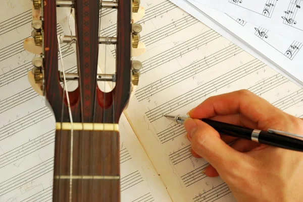 Гитара с рукой, сочиняющая музыку на рукописи — стоковое фото