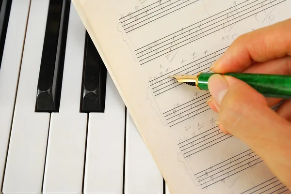 Запись на старую музыкальную партитуру пером на фортепианной клавиатуре — стоковое фото