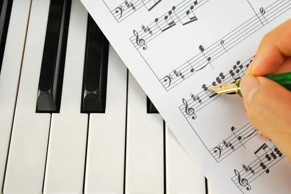 Scrivere su partitura musicale con penna sulla tastiera del pianoforte Foto Stock Royalty Free