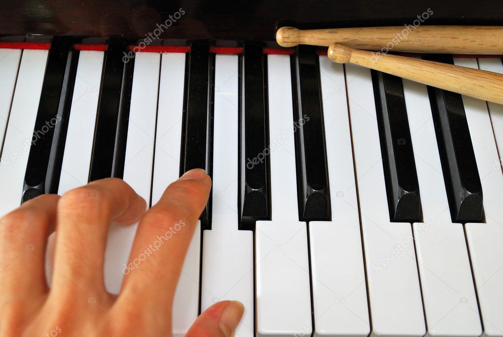 Left hand playing on piano keyboard with drum sticks