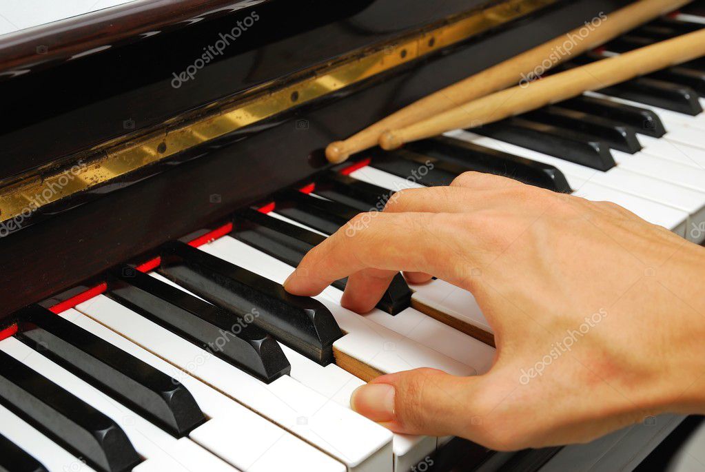 Right hand playing on piano keyboard with drum sticks