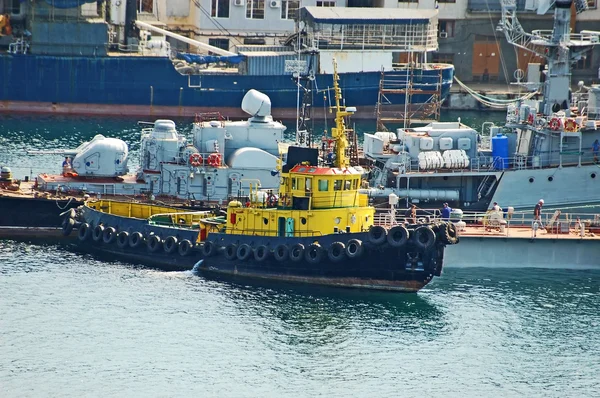 Tugboat at military ship at harbor — Stock Photo, Image