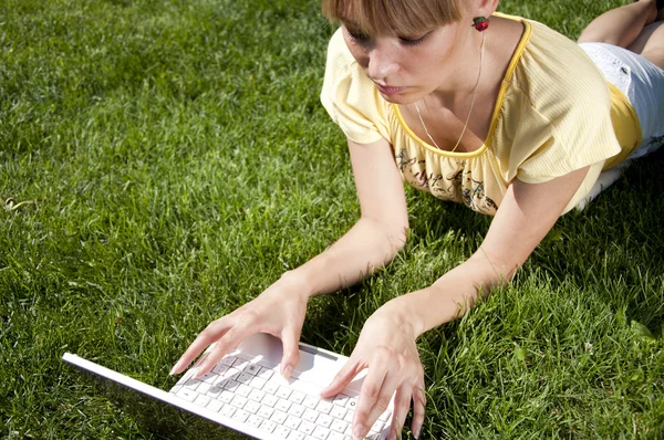 푸른 잔디 위에 노트북을 놓고 앉아 있는 젊은 여자 — 스톡 사진