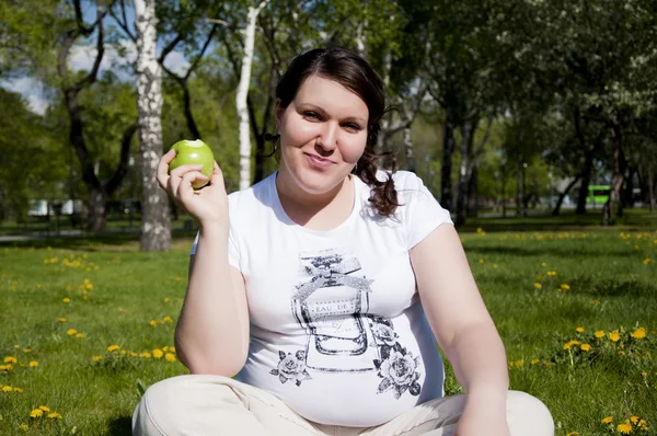 Kobieta siedzi na trawie iwith jabłko — Zdjęcie stockowe
