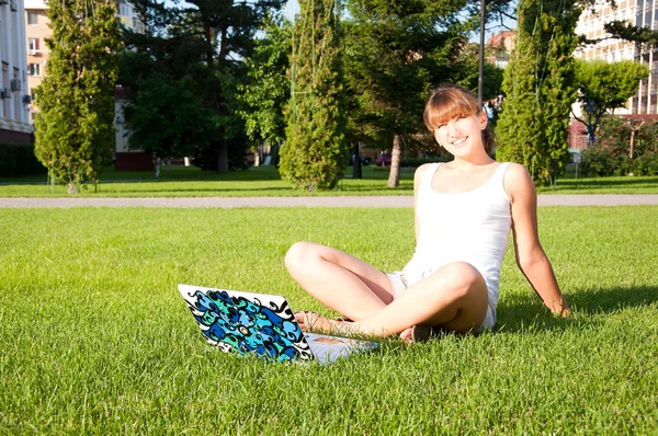 年轻的女孩坐在公园与您的便携式计算机 — 图库照片