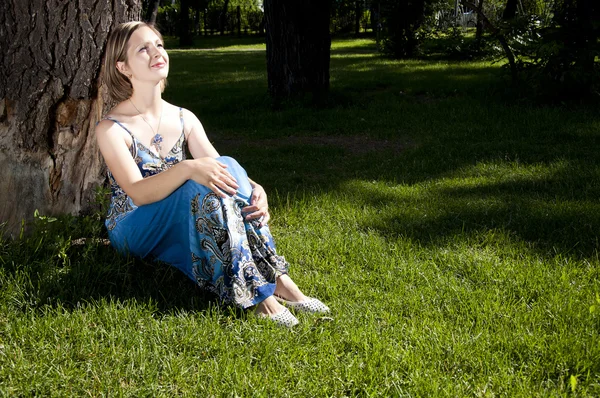 Beautiful woman sitting under a tree in park — Stock Photo, Image