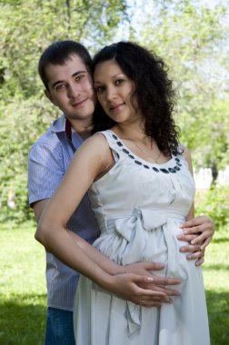 Man and a pregnant woman hugging in the park clipart