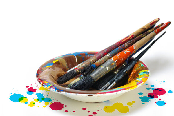 Old dirty painting brushes resting in a colorful plate