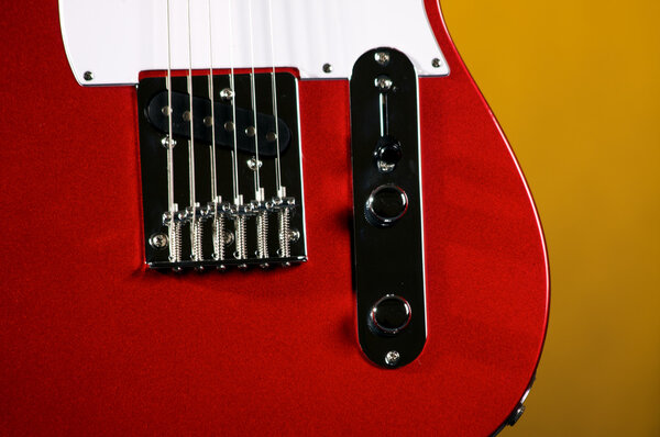 An electric metallic red guitar isolated on a yellow background in the horizontal format with copy space.