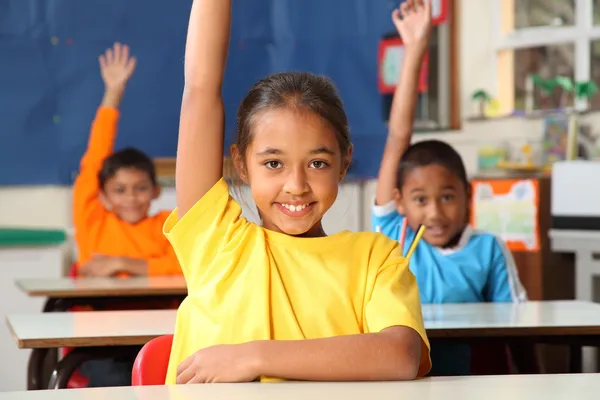 Crianças da escola com as mãos levantadas em sala de aula — Fotografia de Stock