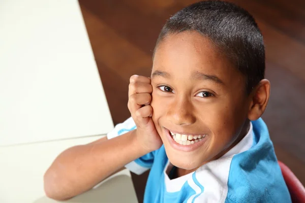 Fiatal iskolás fiú az osztályban íróasztalához ül nevetve — Stock Fotó