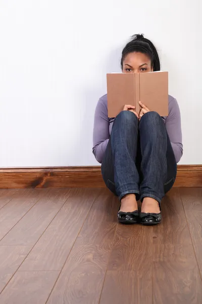 Черная девушка, сидящая на полу за домашней книгой для чтения — стоковое фото