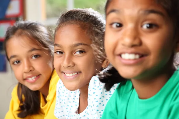 A három fiatal iskolás lányok az osztályban ülve mosolyogva sor — Stock Fotó