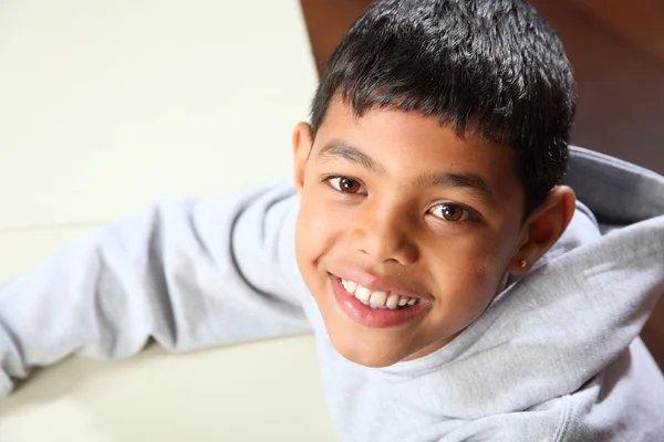 Sonriente joven niño de escuela étnica con capucha gris en el aula — Foto de Stock