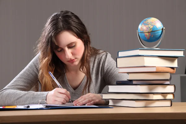 Junges Studentenmädchen schreibt mit Büchern um sich herum — Stockfoto