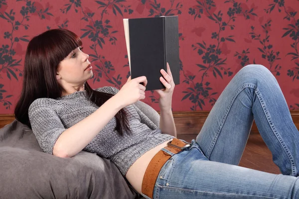 Hübsche junge Frau liegt auf Bohnensack und liest Buch — Stockfoto