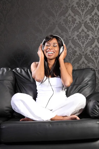 Χαμογελώντας μαύρη γυναίκα στον καναπέ, ακούγοντας μουσική — Φωτογραφία Αρχείου