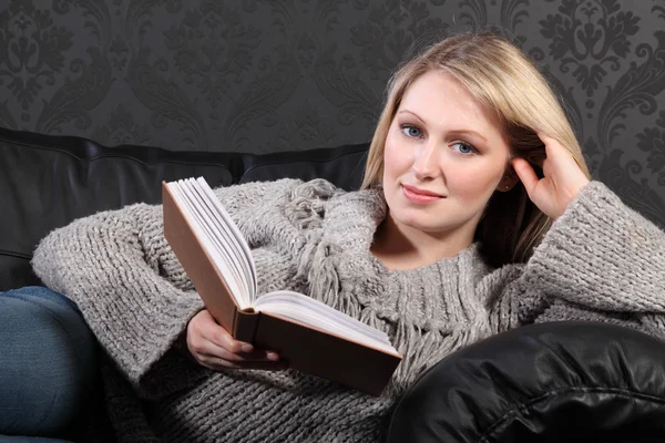 Sarışın kadın rahatlatıcı okuma kitabı ev gülümseyen — Stok fotoğraf