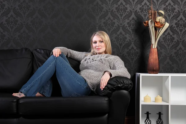 Beautiful blonde woman home on sofa in jumper — Stock Photo, Image