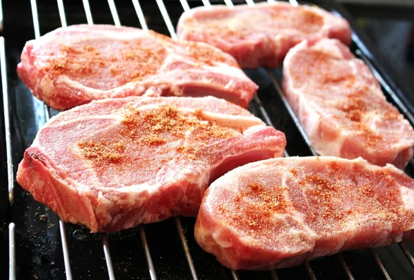 Fett saftige rohe Schweinekoteletts mit Gewürzen überzogen fertig zum Kochen auf Grillblech lizenzfreie Stockfotos