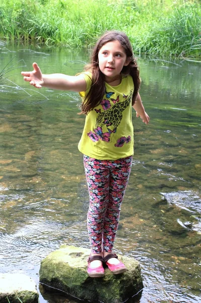 Hübsches Kind greift nach Hilfe, wenn es auf Felsen im Fluss steht Stockbild