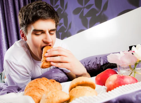 Young male biting croissant bed — Stock Photo, Image
