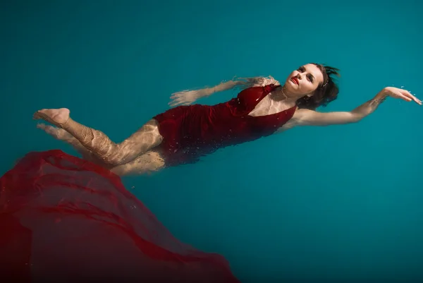 Sexy vrouw drijvend op zwembad in rode jurk — Stockfoto