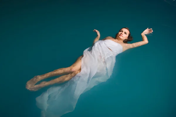 Sexy vrouw drijvend op zwembad in witte jurk — Stockfoto