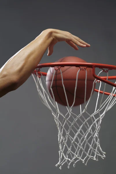 Um homem mergulhando uma bola de basquete através de uma rede com uma mão — Fotografia de Stock