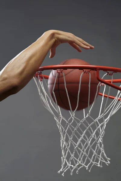 Um homem mergulhando uma bola de basquete através de uma rede com uma mão — Fotografia de Stock