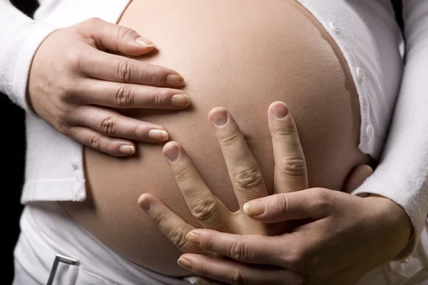 Uma mulher grávida segurando sua barriga com as duas mãos — Fotografia de Stock