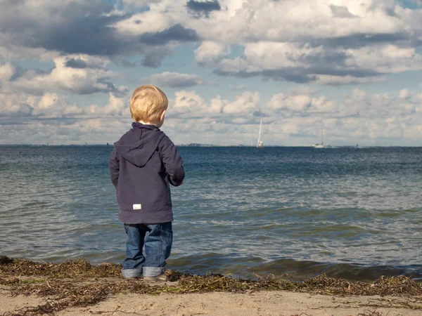 stock image Little boy at a beach looking towards the sea in autumn