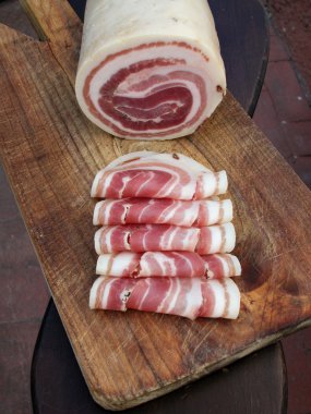 Roll raw bacon with slices on wood trencher clipart