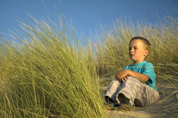 Pojken sitter i sanddynerna — Stockfoto