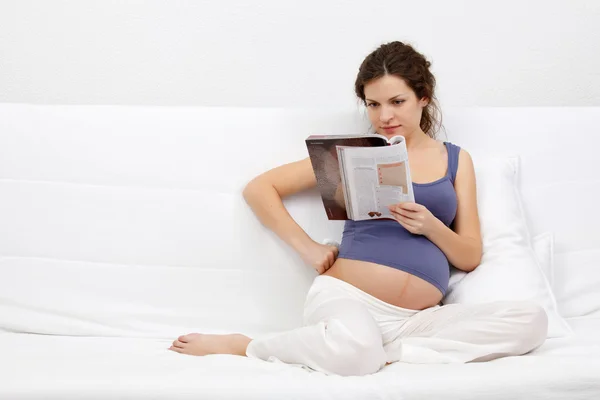 Unga gravid kvinna läser en tidning雑誌を読んで若い妊娠中の女性 — Stockfoto