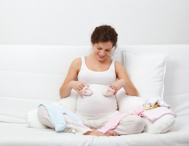 Beautiful pregnant woman choosing baby's clothes clipart