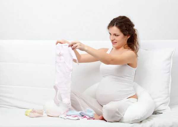 Güzel bir hamile kadın bebeğin giysiler seçmek — Stok fotoğraf