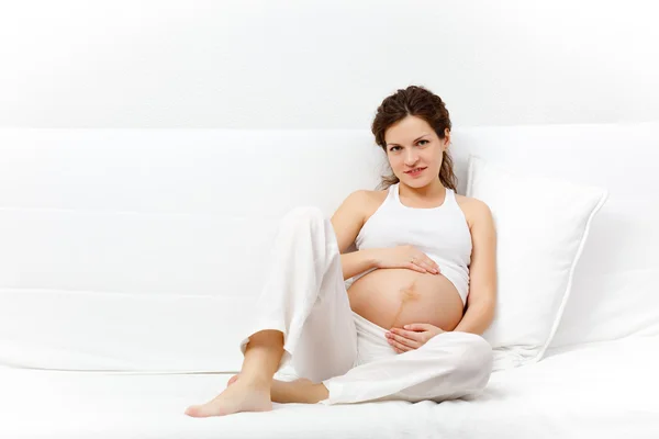 Unga gravid kvinna avkopplande på soffa Royaltyfria Stockbilder