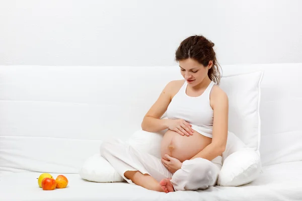 Mujer embarazada joven sentada en el sofá — Foto de Stock