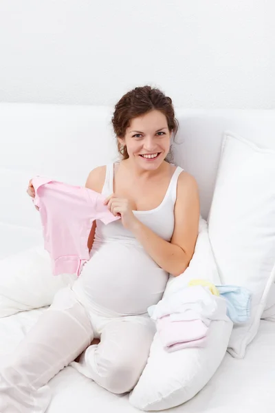 Красивая беременная женщина выбирает одежду для ребенка — стоковое фото