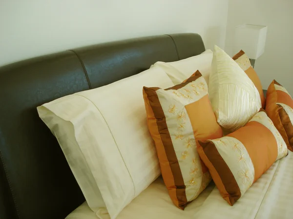 Bruinleren hoofdeinde en oranje kussens op bed — Stockfoto