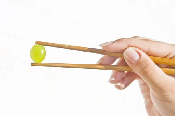 Holding a grape with chinese sticks — Stock Photo, Image